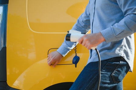 young handsome man holding charging cable at electric charging station point standing near his new car.の写真素材