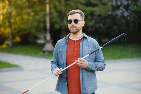 Young handsome blinded man walking with stick in town.