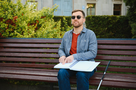 Blind man reading braille book, sitting on bench in summer park, resting.の写真素材