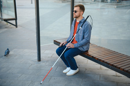 Visually impaired man with walking stick, sitting on bench in city park. copyspace.の写真素材