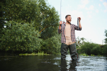 Man with fishing rod, fisherman men in river water outdoor. Catching trout fish in net. Summer...