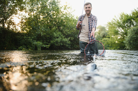 Man with fishing rod, fisherman men in river water outdoor. Catching trout fish in net. Summer...
