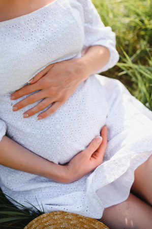 Close-up of pregnant woman with hands on her belly on nature backgroundの写真素材