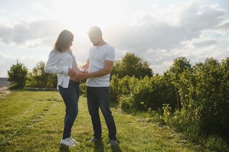 Happy and young pregnant couple hugging in nature.