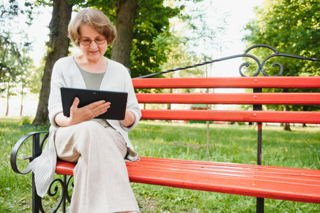 Elegant elderly woman in the shirt is sitting on the bench in a park on a warm day.の写真素材