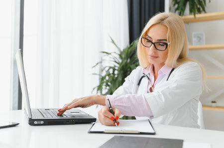 Portrait shot of a middle aged female doctor sitting at a desk and working in a doctor's office.の写真素材