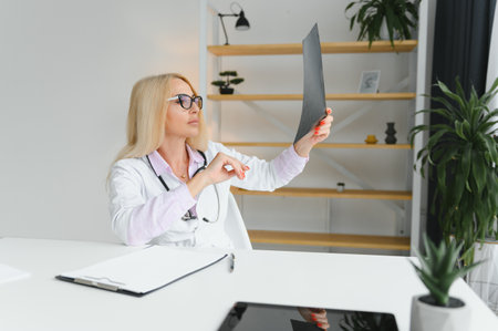 Portrait shot of a middle aged female doctor sitting at a desk and working in a doctor's office.の写真素材