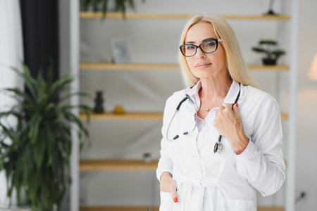 Female doctor wearing lab coat and stethoscope and holding clipboard in her hands while standing at hospitalの写真素材