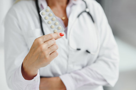 Smiling middle aged female therapist in white uniform holds pillsの写真素材