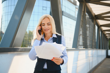 Business Woman With Phone Near Office. Portrait Of Beautiful Smiling Female In Fashion Office Clothes Talking On Phone While Standing Outdoors. phone communication. High Quality Imageの写真素材