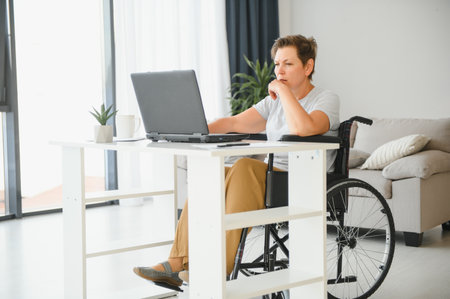 Positive elderly woman in wheelchair working on laptop, IT freelancer, online.