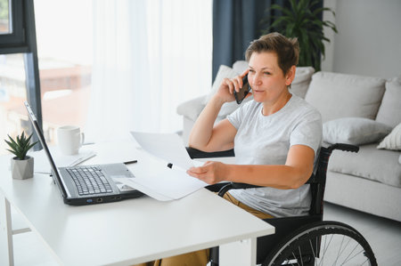 Middle age woman using laptop sitting on wheelchair at home.