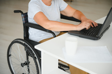 Middle age woman using laptop sitting on wheelchair at home.の写真素材