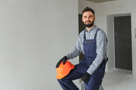Portrait of handsome mechanic with stubble in blue overall, shirt having his arms crossed, looking...