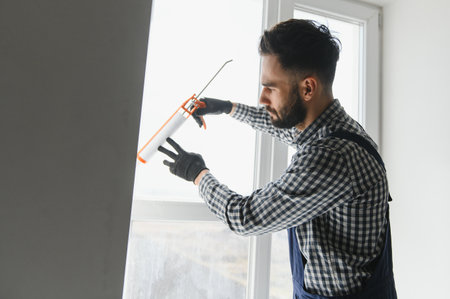 Contractor hand holding glue gun with silicone to repair tile and window. Installation or renovation interior conceptの写真素材