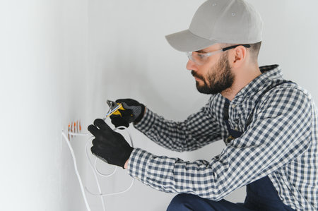 Professional electrician working on a home electrical system, he is installing a wall socket.