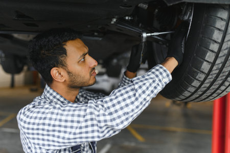 Indian car mechanic standing and working in service station. Car specialists examining the lifted car. Professional repairmen wearing mechanic uniform in blue colorの写真素材