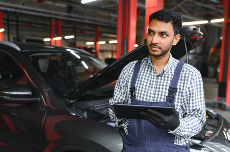Mechanic man mechanic manager worker using a laptop computer checking car in workshop at auto car repair service center. Engineer young man looking at inspection vehicle details under car hoodの写真素材
