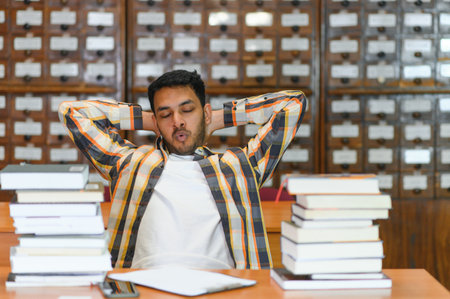 Portrait of cheerful male international Indian student with backpack, learning accessories standing near bookshelves at university library or book store during break between lessons. education concept.の写真素材