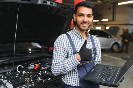 Indian car mechanic standing and working in service station. Car specialists examining the lifted car. Professional repairmen wearing mechanic uniform in blue colorの写真素材