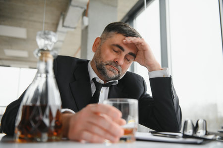 Alcoholism at work. Tired employee drinking alcohol at workplace, can not handle stress.の写真素材