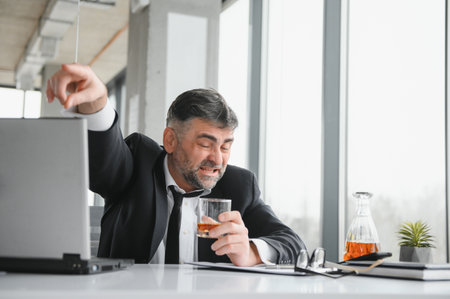 Alcoholism at work. Tired employee drinking alcohol at workplace, can not handle stress.の写真素材