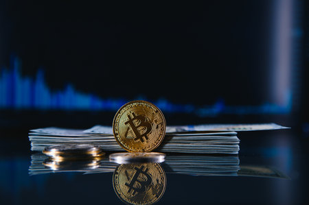 Golden bitcoins are stacked on a bright background of business graphs close-up. bitcoin cryptocurrency. Folded in a tube 100 dollar bills.の写真素材