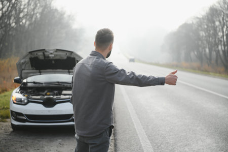 A young man near a broken car with an open hood on the roadsideの写真素材