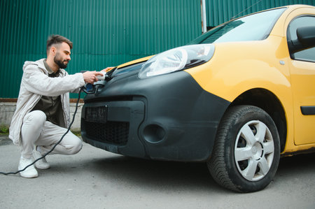Man Holding Power Charging Cable For Electric Car In Outdoor Car Park. And he's going to connect the car to the charging station in the parking lot near the shopping center.の写真素材