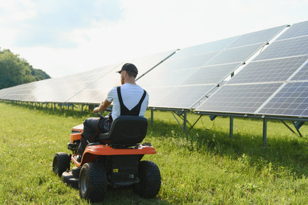 A man drives a lawnmower near solar panels. Concept of solar energy.の写真素材