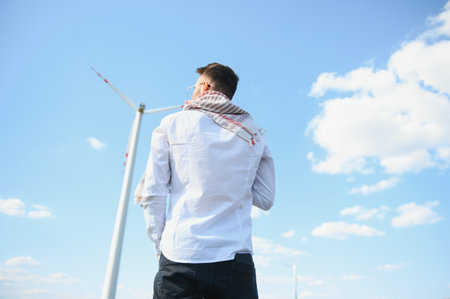 Arab man standing with wind turbine on mountain.