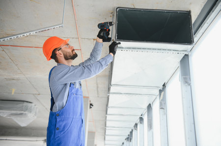 Industrial Theme. Warehouse Heating and Cooling System Installation by Professional Caucasian Technician. Commercial Building Ventilation Rectangle Canals. Air distributionの写真素材