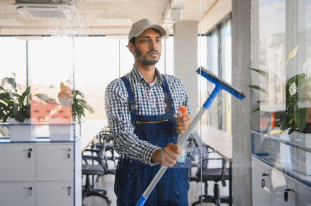 Young indian man washing window in office.の写真素材