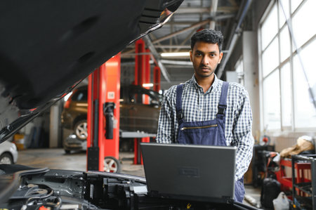Indian car mechanic standing and working in service station. Car specialists examining the lifted car. Professional repairmen wearing mechanic uniform in blue colorの写真素材
