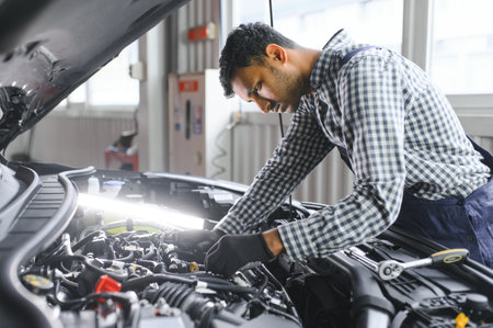 Indian car mechanic standing and working in service station. Car specialists examining the lifted car. Professional repairmen wearing mechanic uniform in blue colorの写真素材