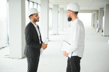 Multiracial male coworkers in hardhats discussing project on construction site.