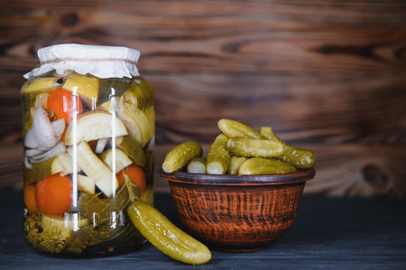 Glass jars with pickled cucumbers (pickles), pickled tomatoes and cabbage. Jars of various pickled vegetables. Canned food in a rustic compositionの写真素材