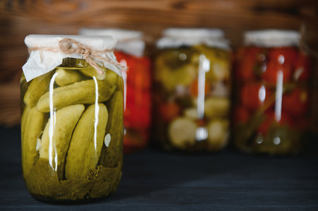 Glass jars with pickled cucumbers (pickles), pickled tomatoes and cabbage. Jars of various pickled vegetables. Canned food in a rustic compositionの写真素材