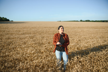 Woman farmer agronomist working in grain field and planning income of harvest. Female examining and checking quality control of produce wheat crop. agriculture management and agribusiness.の写真素材