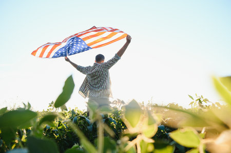 A young farmer stands with a USA flag in a soybean field. The concept of the US agricultural...