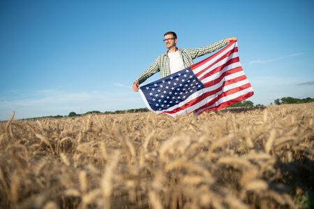Young patriotic farmer stands among new harvest. Boy walking with the american flag on the wheat field celebrating national independence day. 4th of July conceptの写真素材