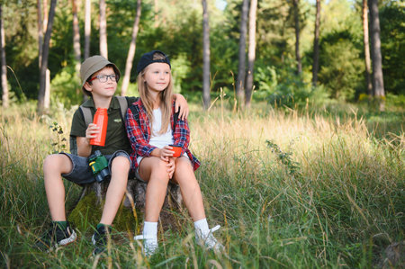 Two happy children having fun during forest hike on beautiful day in pine forest. Cute boy scout with binoculars during hiking in summer forest. Concepts of adventure, scouting and hiking tourism.の写真素材