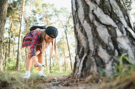 Rear view image of cute little girl exploring the nature with magnifying glass outdoor. Child playing in the forest with magnifying glass. Curious kid looking through magnifier to the tree in the parkの写真素材