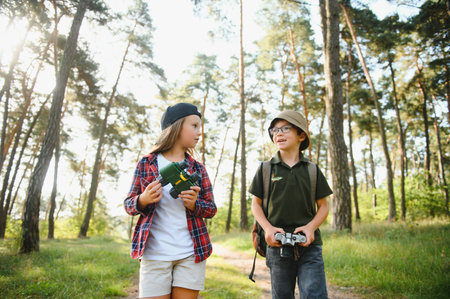 Happy excited school children with backpacks in casual clothes enjoying walk in forest on sunny autumn day, two active kids boy and girl running and playing together during camping trip in natureの写真素材