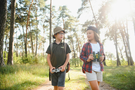Happy excited school children with backpacks in casual clothes enjoying walk in forest on sunny autumn day, two active kids boy and girl running and playing together during camping trip in natureの写真素材