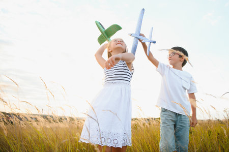 Running boy and girl holding two green and blue airplanes toy in the field during summer sunny day.の写真素材