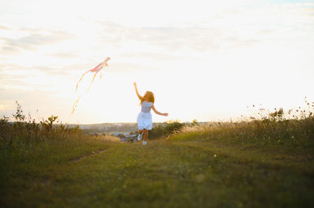 happy child girl with a kite running on meadow in summer in nature.の写真素材