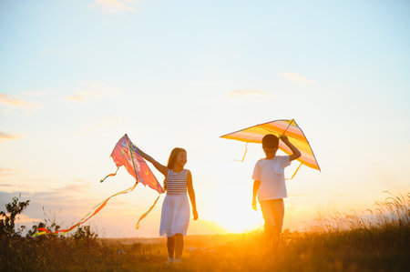 Brother and sister playing with kite and plane at the field on the sunsetの写真素材