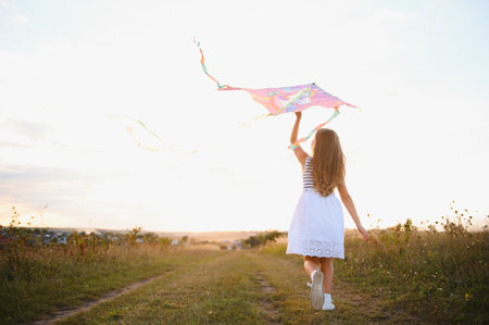 happy child girl with a kite running on meadow in summer in nature.の写真素材