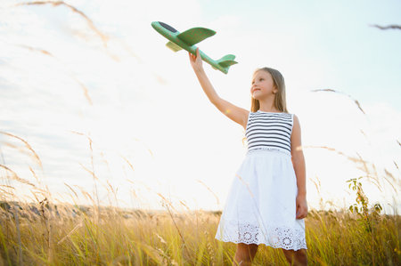 Happy girl runs with a toy airplane on a field in the sunset light. children play toy airplane. teenager dreams of flying and becoming a pilot. girl wants to become a pilot and astronaut. slow motionの写真素材